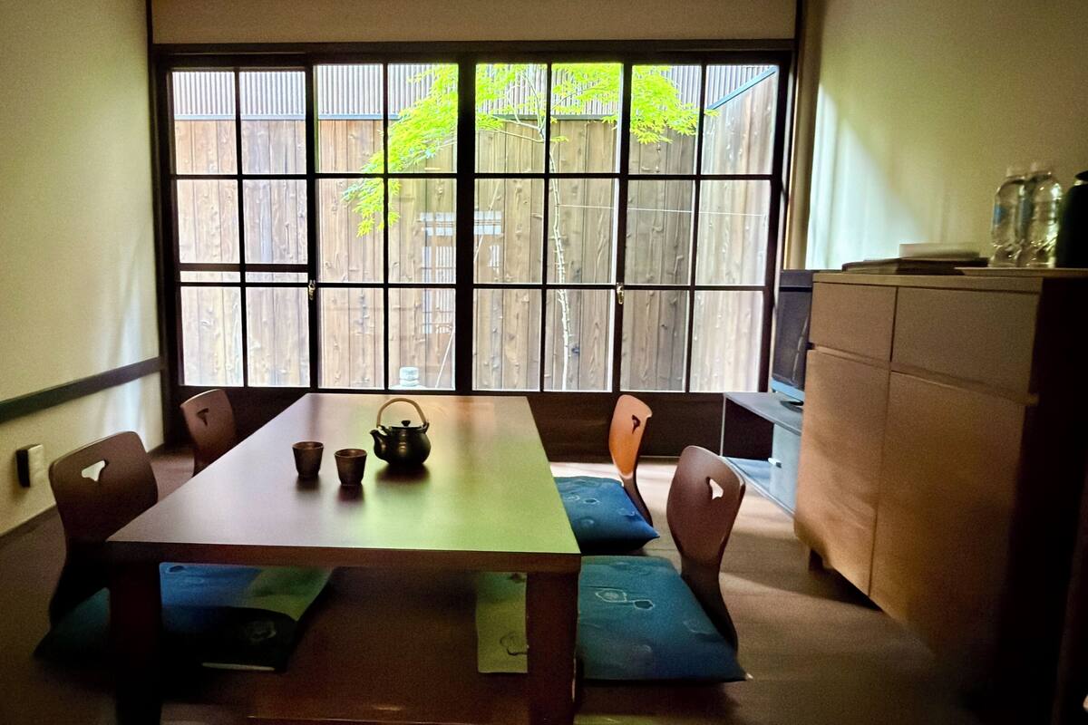 A dining area with a table, chairs, a window with a view of a wooden fence, and a cabinet.