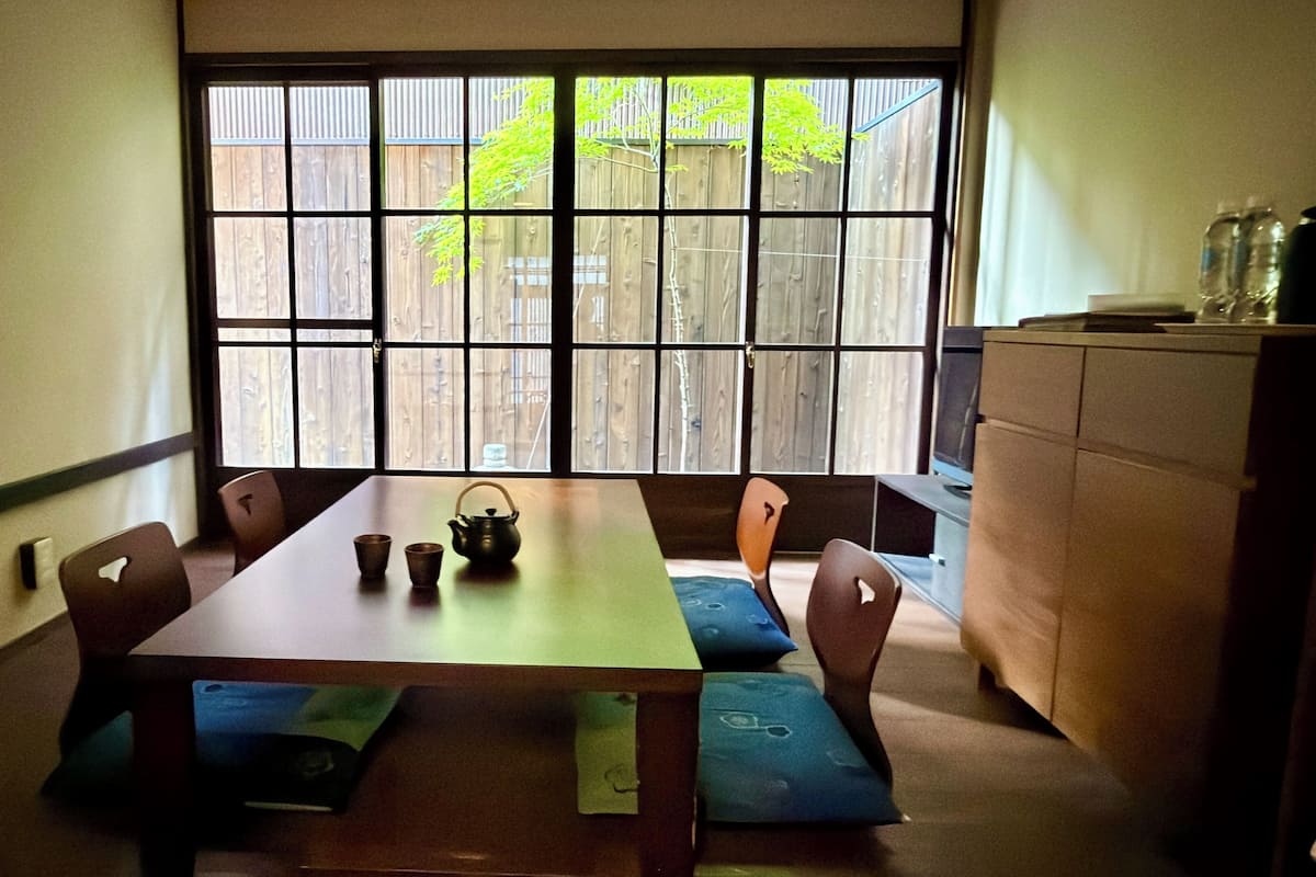 Un comedor con una mesa, sillas, un ventanal con vista a una valla de madera y un armario.
