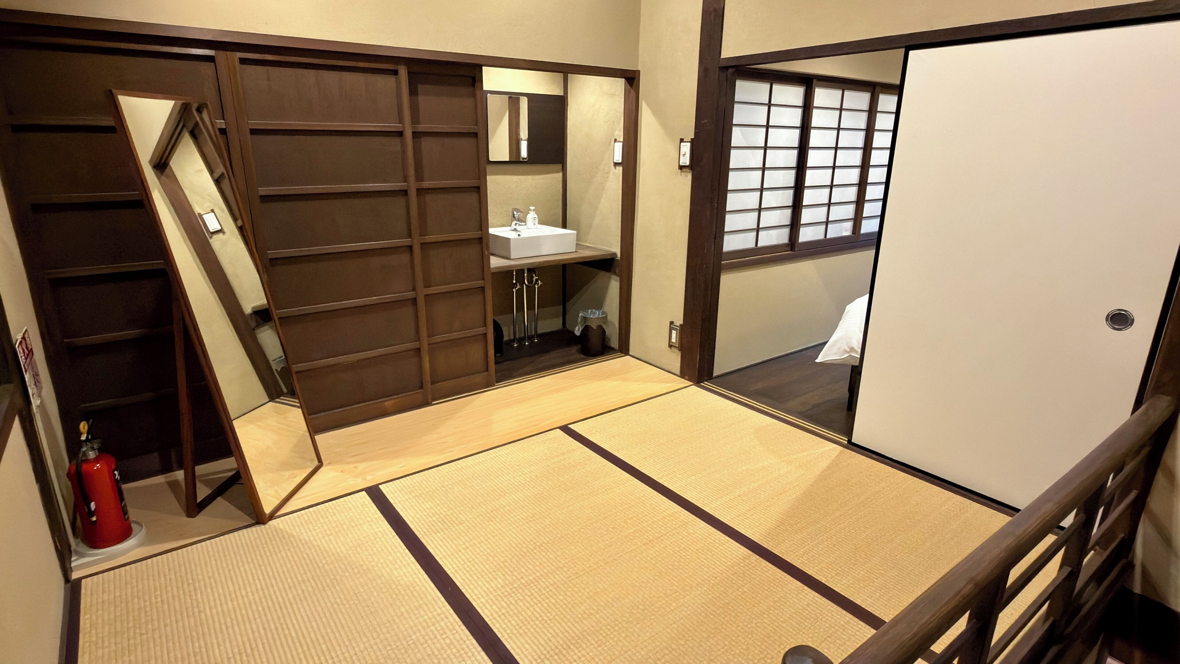 A traditional Japanese room with tatami flooring, a sliding door, a small sink, and a mirror.