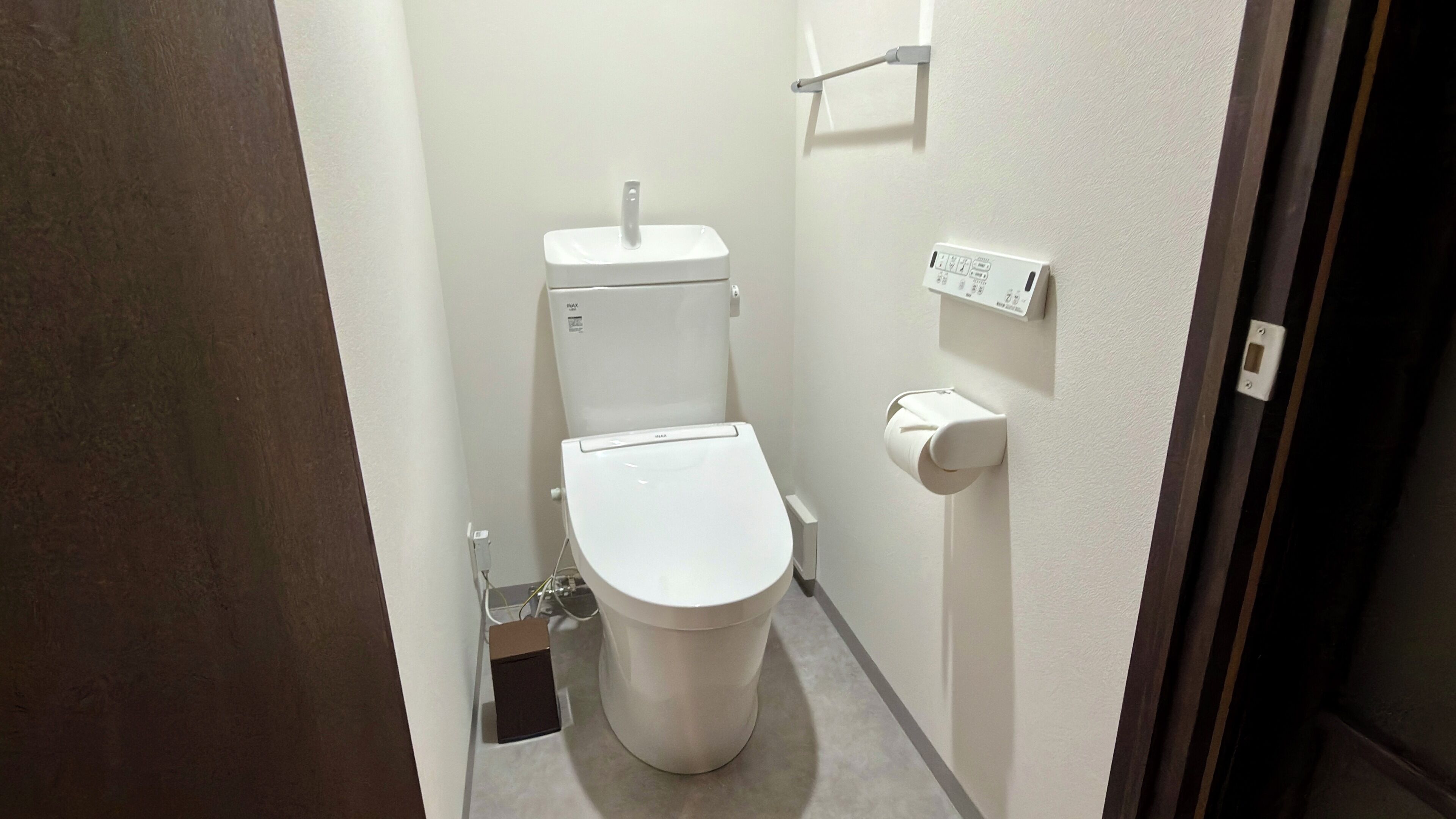 Un baño pequeño y blanco con un inodoro, un secador de manos y un enchufe en la pared.