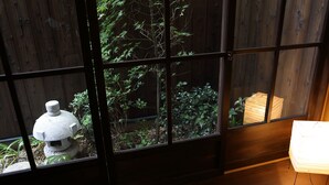 Una habitación con vistas a través de una ventana con marco de madera, un farol de piedra y una pila de papeles en el suelo.