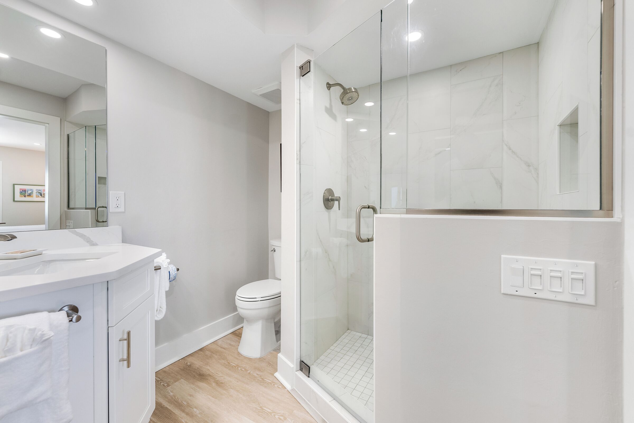 Un baño moderno con ducha envuelta en vidrio, inodoro blanco y tocador con espejo.