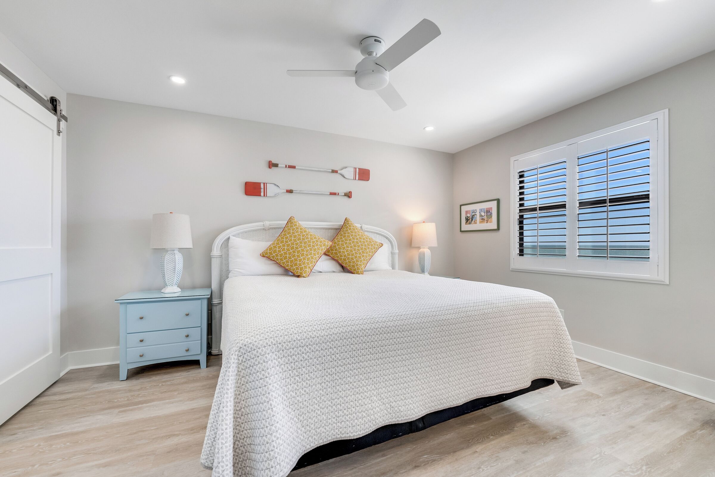 A bedroom with a bed, nightstand, lamp, ceiling fan, and window with blinds.