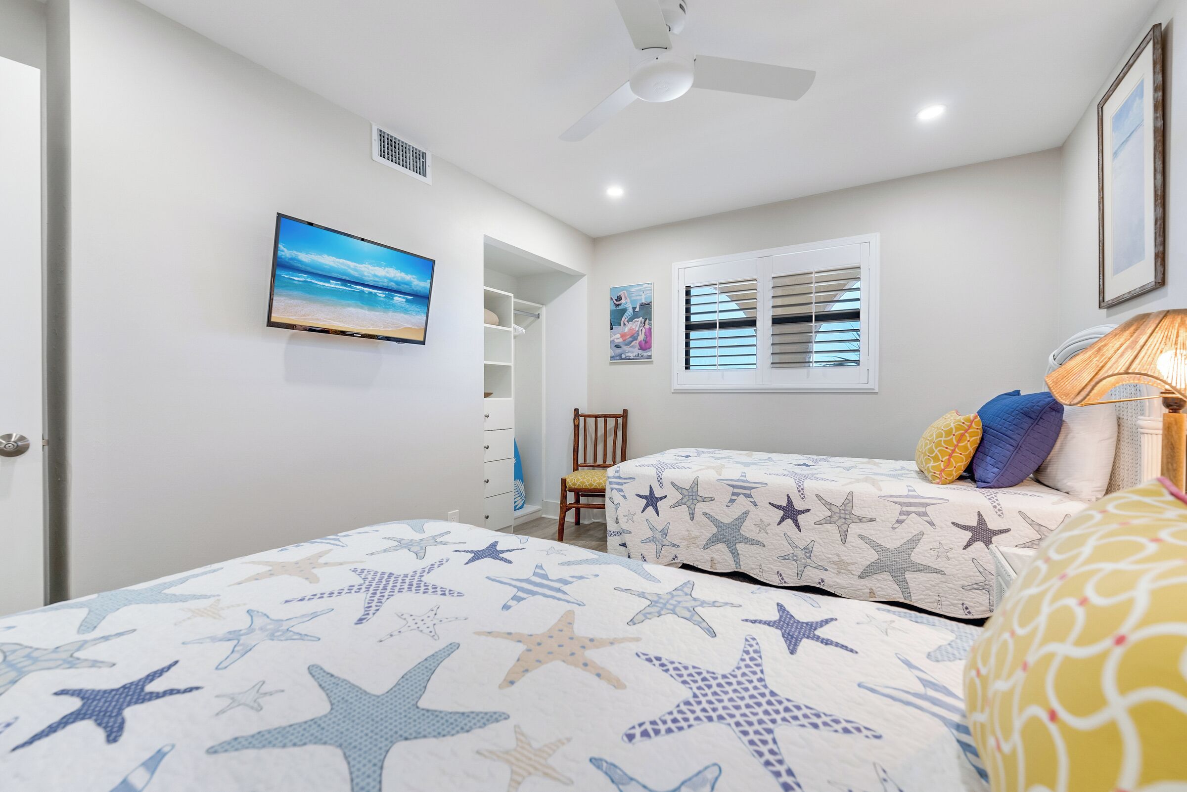A bedroom with two beds, a ceiling fan, a window with blinds, a TV, and a bookshelf.