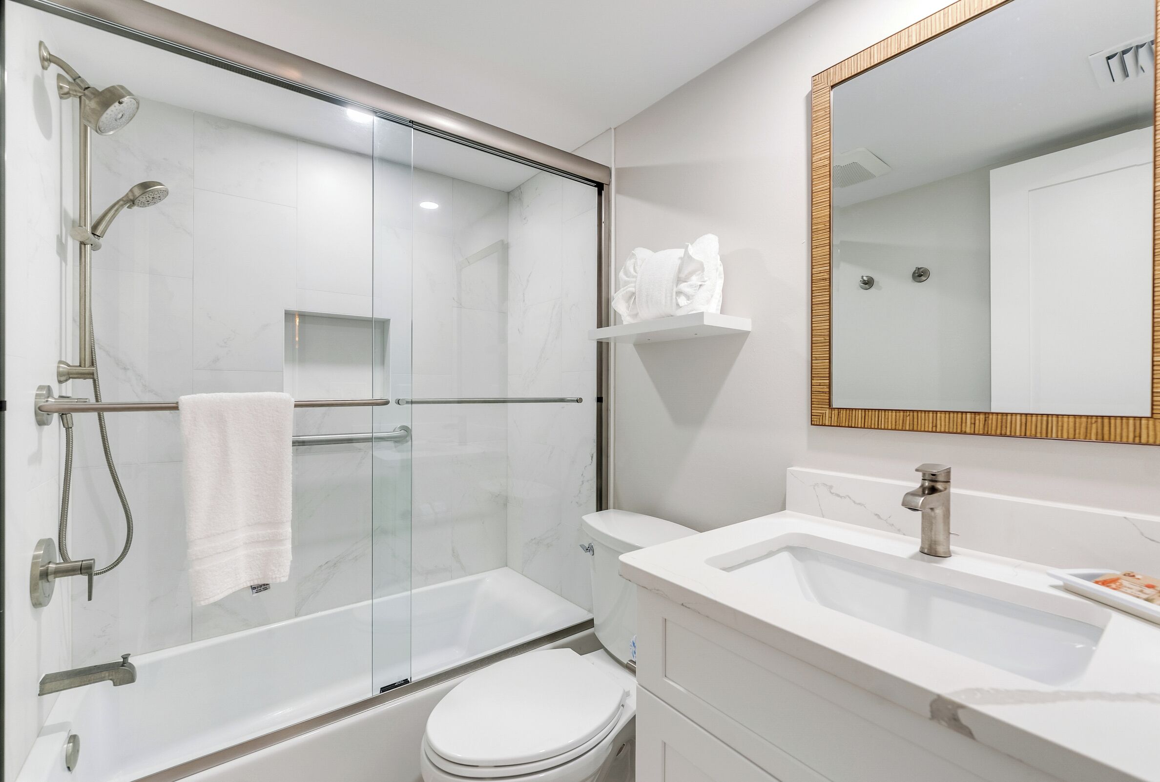 Une salle de bain moderne avec une douche à parois de verre, des toilettes blanches, un lavabo avec un miroir et un porte-serviettes.