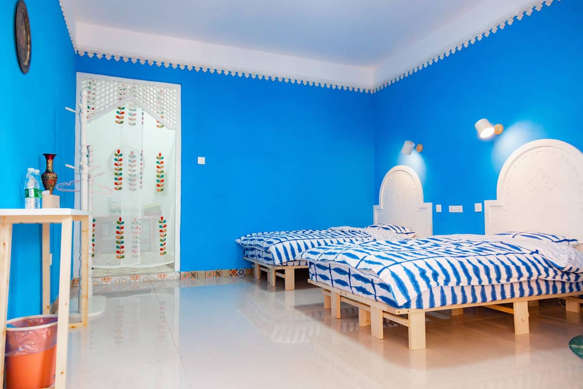 Quarto com duas camas, um guarda-roupa branco, uma mesinha e um espelho.