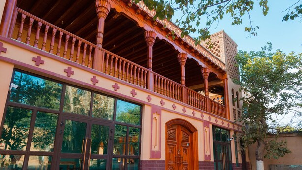 A building with a balcony, large windows, and a wooden door. - New Dap Hostel in Grape Town (Turpan)