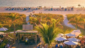 A beachside restaurant with outdoor seating, a stage for live music, and a view of the beach and ocean. - What a View! Low Rates! 5-STAR! Waterfront, 2BR, private balcony, walk to Beach! (Treasure Island)