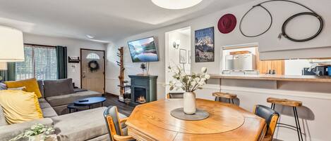 A modern living room with a wooden dining table, comfortable seating, a fireplace, and a TV mounted on the wall.