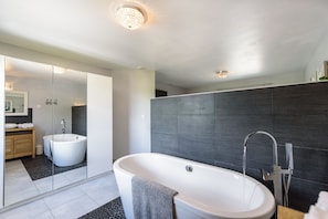 Ein modernes Badezimmer mit einer freistehenden Badewanne, einem großen Spiegel und dunklen Fliesenwänden.