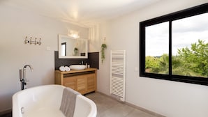 Un baño moderno con una bañera independiente, un tocador de madera, un espejo grande y un ventanal con vista a zonas verdes.