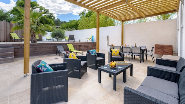 Un patio al aire libre con mobiliario de mimbre, una pérgola de madera y suelo de baldosas de piedra.