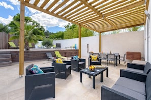 Un patio al aire libre con mobiliario de mimbre, una pérgola de madera y suelo de baldosas de piedra.