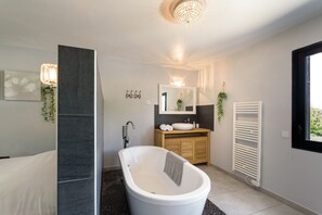 Un baño moderno con una bañera independiente, un tocador de madera, un espejo y un radiador.