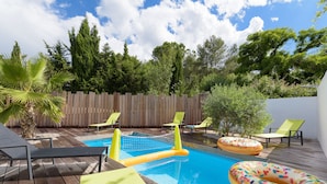 Una terraza de madera con piscina, flotadores hinchables y sillones de descanso.