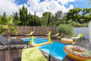 Una terraza de madera con piscina, flotadores hinchables y sillones de descanso.