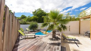 Una terraza de madera con sillones de descanso, una piscina pequeña y una palmera.