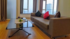 Una sala de estar moderna con un sofá, una mesa de centro de vidrio y vistas a un paisaje urbano a través de grandes ventanales.