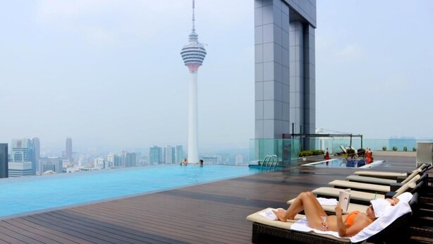 Piscina infinita en la azotea con sillas de descanso y vista a una torre.