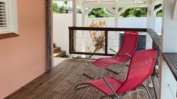 Un espace extérieur abrité, doté d’une terrasse en bois, de deux chaises rouges et offrant une vue sur la verdure.