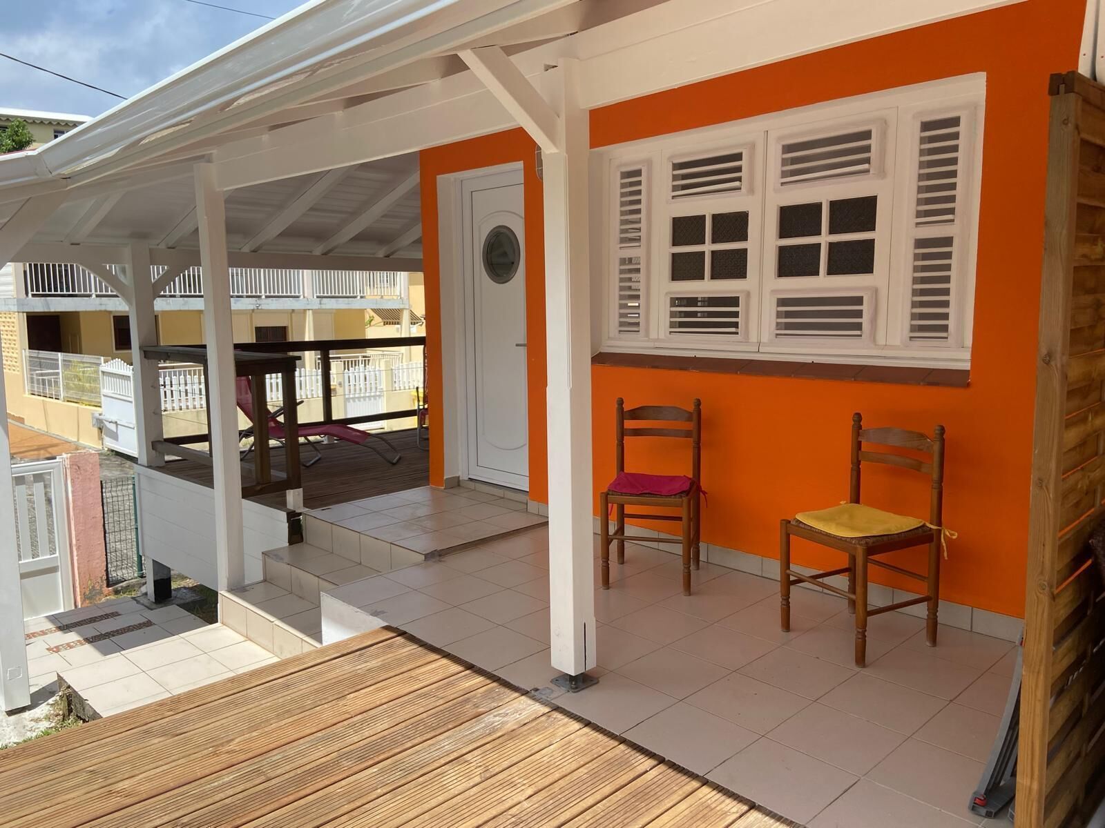 A covered outdoor area with a wooden deck, two wooden chairs, and a white door.
