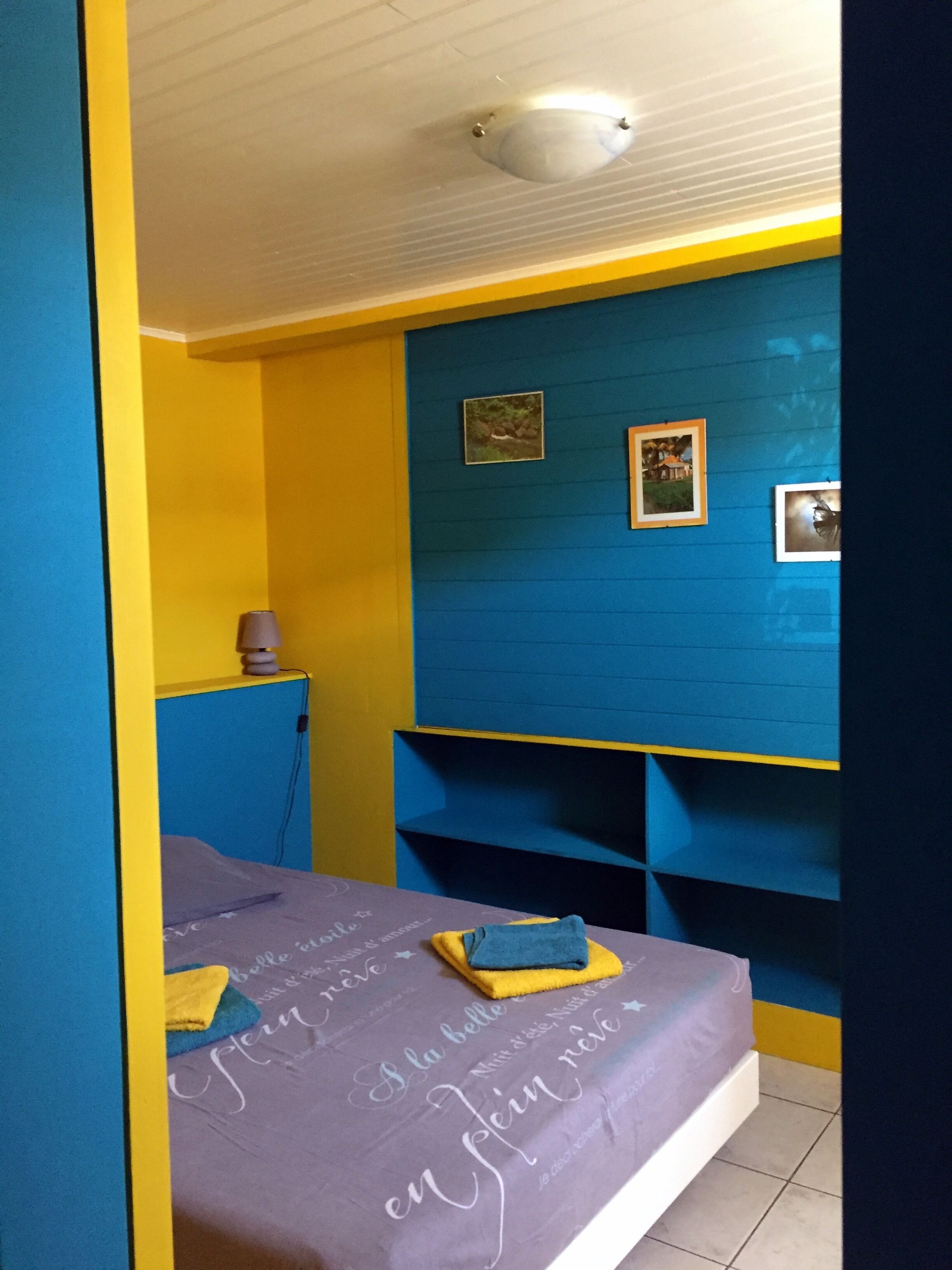 Une chambre à coucher avec un lit, une table de chevet et une étagère fixée au mur.