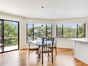 A dining area with a glass table and chairs, large windows, and a view of trees and buildings. - The Treehouse on Lake Travis (Lakeway)