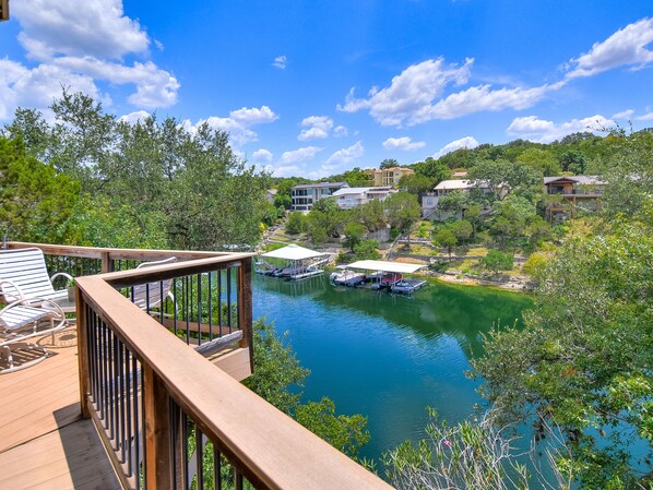 A wooden deck overlooking a lake with boats, surrounded by greenery and houses. - The Treehouse on Lake Travis (Lakeway)