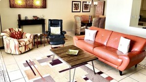 Ein Wohnzimmer mit einem roten Ledersofa, einem gemusterten Sessel, einem schwarzen Sessel, einem Holztisch und einem Deckenventilator.