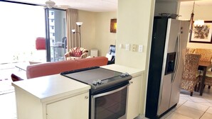 Eine kompakte Küche mit Einbauofen, Kühlschrank und einer Essecke mit Korbstuhl-Tisch und -Stühlen.