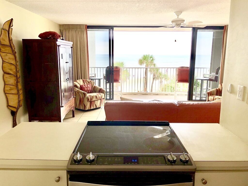 A room with a view of the ocean, a dining table, a sofa, and a cabinet.