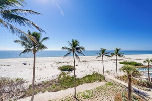 A beach with palm trees, a sandy path, and a pool area. - OCEAN'S REACH 1C4: Top Floor, Gulf-Front View, Washer/Dryer, Amenities Open! (Sanibel Island)
