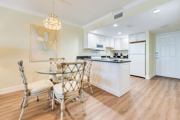 A modern kitchen with white cabinets, a central island, and a dining area with wicker chairs. - OCEAN'S REACH 1C4: Top Floor, Gulf-Front View, Washer/Dryer, Amenities Open! (Sanibel Island)