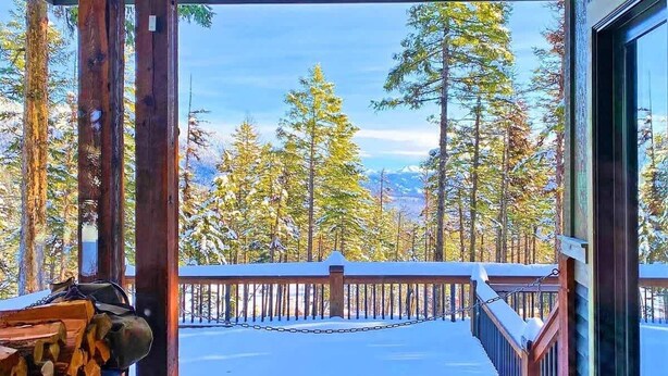 A wooden deck with a view of snow-covered trees and mountains.