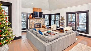 A modern living room with a stone fireplace, large windows, and a Christmas tree.
