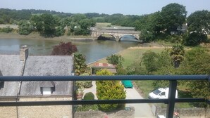 A view of a river with a bridge, a stone building, and a car parked in the foreground.