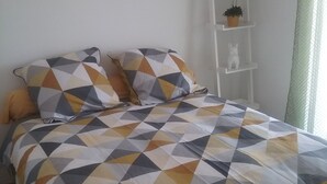 A bed with a geometric patterned bedspread, a white shelf with a potted plant, and a small figurine.