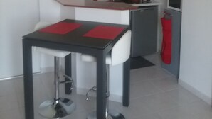 A compact kitchen with a dining area, featuring a modern design with a central island, white and grey cabinetry, and a red accent wall.