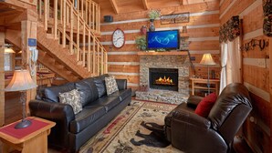 A log cabin interior with a fireplace, leather sofas, a wooden staircase, and a television. - Bare Snugglin' 1 bedroom, sleeps 4! (Sevierville)