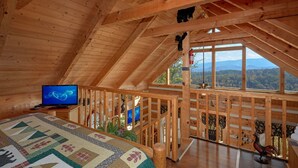 A wooden cabin with a high ceiling, a television, a quilted bed, and a view of the mountains. - Bare Snugglin' 1 bedroom, sleeps 4! (Sevierville)