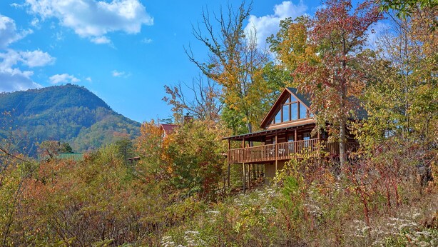 A cabin with a wooden deck and large windows, surrounded by autumn foliage and a mountain in the background. - Bare Snugglin' 1 bedroom, sleeps 4! (Sevierville)