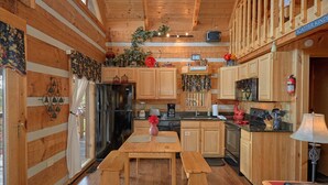 A cabin-style kitchen with wooden cabinets, a refrigerator, a stove, and a dining area with benches. - Bare Snugglin' 1 bedroom, sleeps 4! (Sevierville)