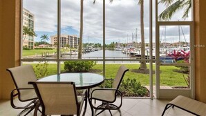 Ein Zimmer mit Glastisch und Stühlen, Blick auf eine Marina mit Booten und eine Palme draußen.