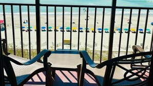 A balcony with a view of a beach and the ocean. There are several beach umbrellas and chairs on the beach. - Azure Bliss. Oceanfront Condo. Sleeps 6. (Myrtle Beach)