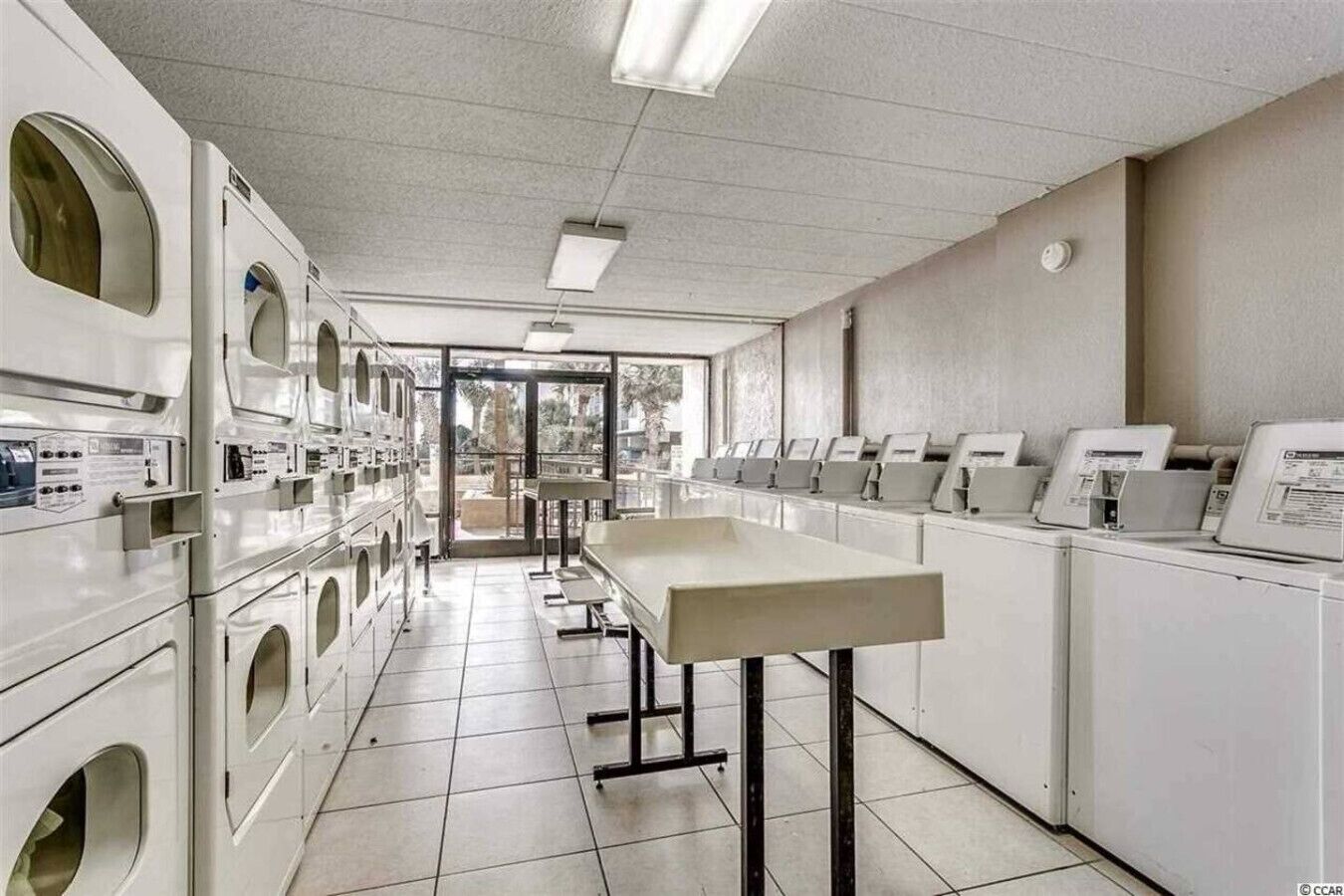 A laundry facility with multiple washing machines and dryers, a long counter, and a tiled floor.