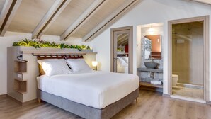 A modern bedroom with a large bed, wooden beams on the ceiling, a bedside plant arrangement, a built-in shelf, and a bathroom with a glass shower. - 1924 suites  Terrace (Chania)