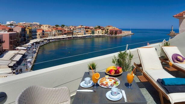A dining table with breakfast items and a view of a coastal town. - 1924 suites  Terrace (Chania)