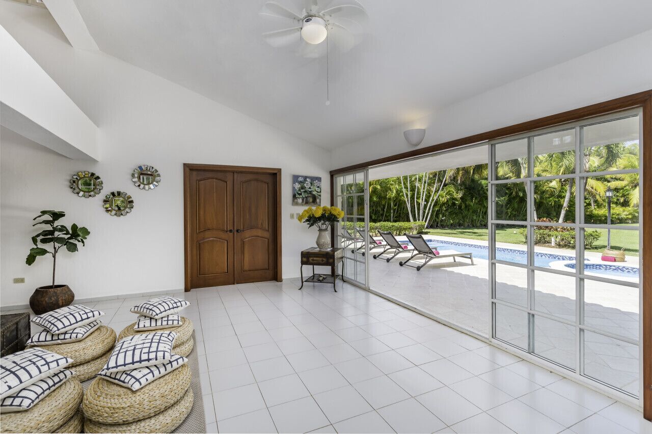 A spacious room with a large sliding glass door leading to a pool area, a ceiling fan, and a wooden door.