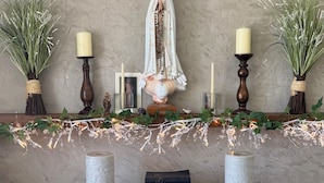 En religiøs figur med stearinlys, en rosenkrans og bøger på en hylde.