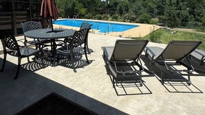 En udendørs terrasse med pool, liggestole og et bord med stole.